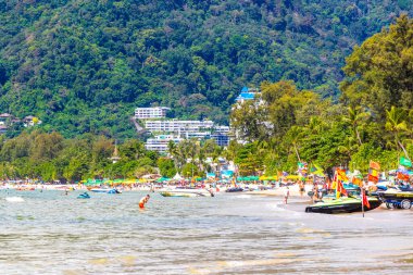 Kathu Phuket Tayland 13 numara. Ekim 2025 Patong Sahili manzaralı gezinti turistleri mavi su dalgaları güneş şemsiyeleri cankurtaran kuleleri dağlar ve Tayland palmiyeleri.