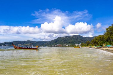 Kathu Phuket Tayland 13 numara. Ekim 2025 Patong Sahili manzaralı gezinti turistleri mavi su dalgaları güneş şemsiyeleri cankurtaran kuleleri dağlar ve Tayland palmiyeleri.