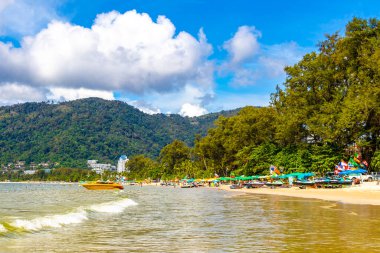 Kathu Phuket Tayland 13 numara. Ekim 2025 Patong Sahili manzaralı gezinti turistleri mavi su dalgaları güneş şemsiyeleri cankurtaran kuleleri dağlar ve Tayland palmiyeleri.