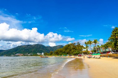 Kathu Phuket Tayland 13 numara. Ekim 2025 Patong Sahili manzaralı gezinti turistleri mavi su dalgaları güneş şemsiyeleri cankurtaran kuleleri dağlar ve Tayland palmiyeleri.