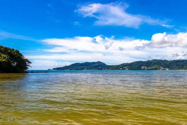 Patong Beach bay sea coast panorama view with turquoise blue clear water waves white sand and green mountains and palm trees in Patong Beach Kathu District Phuket Island Province Southern Thailand.