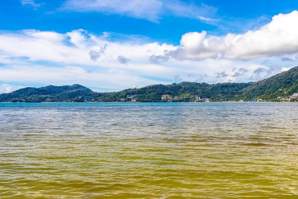 Patong Beach bay sea coast panorama view with turquoise blue clear water waves white sand and green mountains and palm trees in Patong Beach Kathu District Phuket Island Province Southern Thailand.