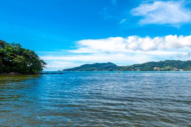 Patong Beach bay sea coast panorama view with turquoise blue clear water waves white sand and green mountains and palm trees in Patong Beach Kathu District Phuket Island Province Southern Thailand.