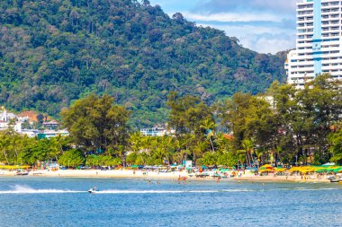 Kathu Phuket Tayland 13 numara. Ekim 2025 Patong Sahili manzaralı gezinti turistleri mavi su dalgaları güneş şemsiyeleri cankurtaran kuleleri dağlar ve Tayland palmiyeleri.