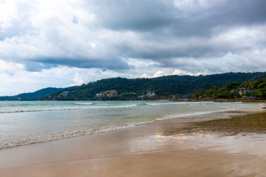 Patong Beach bay sea coast panorama view with turquoise blue clear water waves white sand and green mountains and palm trees in Patong Beach Kathu District Phuket Island Province Southern Thailand.