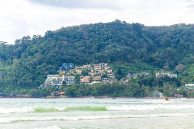 Patong Beach bay sea coast panorama view with turquoise blue clear water waves white sand and green mountains and palm trees in Patong Beach Kathu District Phuket Island Province Southern Thailand.