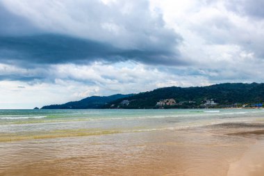 Patong Beach bay sea coast panorama view with turquoise blue clear water waves white sand and green mountains and palm trees in Patong Beach Kathu District Phuket Island Province Southern Thailand.