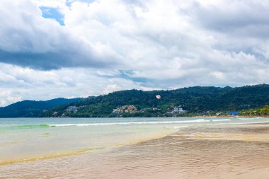 Patong Beach bay sea coast panorama view with turquoise blue clear water waves white sand and green mountains and palm trees in Patong Beach Kathu District Phuket Island Province Southern Thailand.