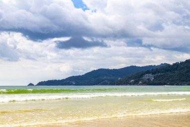 Patong Beach bay sea coast panorama view with turquoise blue clear water waves white sand and green mountains and palm trees in Patong Beach Kathu District Phuket Island Province Southern Thailand.