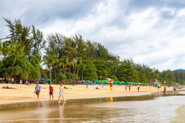 Kathu Phuket Tayland 17 numara. Ekim 2025 Patong Sahili manzaralı gezinti turistleri mavi su dalgaları güneş şemsiyeleri cankurtaran kuleleri dağlar ve Tayland palmiyeleri.
