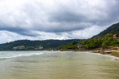 Patong Beach bay sea coast panorama view with turquoise blue clear water waves white sand and green mountains and palm trees in Patong Beach Kathu District Phuket Island Province Southern Thailand.