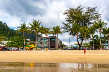 Kathu Phuket Tayland 17 numara. Ekim 2025 Patong Sahili manzaralı gezinti turistleri mavi su dalgaları güneş şemsiyeleri cankurtaran kuleleri dağlar ve Tayland palmiyeleri.