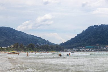 Kathu Phuket Tayland 17 numara. Ekim 2025 Patong Sahili sahil manzaralı gezinti turistleri açık mavi su dalgaları ve yeşil dağlar ve Patong Tayland 'daki palmiye ağaçları..