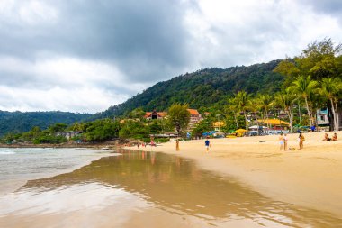 Kathu Phuket Tayland 17 numara. Ekim 2025 Patong Sahili manzaralı gezinti turistleri mavi su dalgaları güneş şemsiyeleri cankurtaran kuleleri dağlar ve Tayland palmiyeleri.