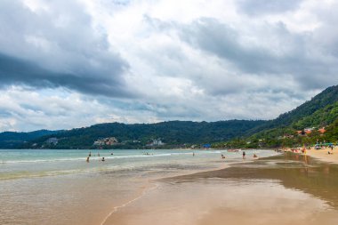Kathu Phuket Tayland 17 numara. Ekim 2025 Patong Sahili sahil manzaralı gezinti turistleri açık mavi su dalgaları ve yeşil dağlar ve Patong Tayland 'daki palmiye ağaçları..