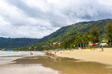 Kathu Phuket Tayland 17 numara. Ekim 2025 Patong Sahili manzaralı gezinti turistleri mavi su dalgaları güneş şemsiyeleri cankurtaran kuleleri dağlar ve Tayland palmiyeleri.