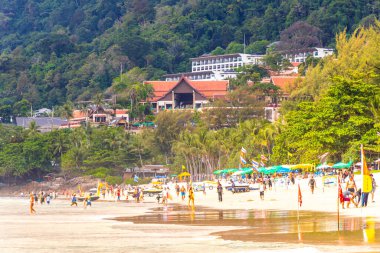 Kathu Phuket Tayland 17 numara. Ekim 2025 Patong Sahili manzaralı gezinti turistleri mavi su dalgaları güneş şemsiyeleri cankurtaran kuleleri dağlar ve Tayland palmiyeleri.