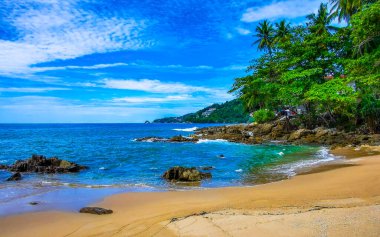 İnanılmaz kayalık Kalim Sahili tropikal manzara manzarası mavi gökyüzü turkuvaz su dalgaları palmiye ağaçları ve kayalar Patong Sahili Kathu Phuket Adası Güney Tayland.