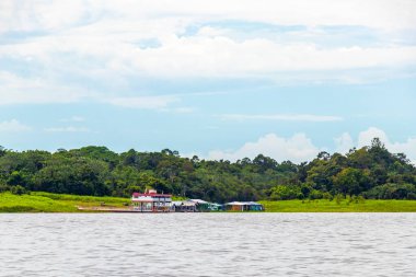 Amazon Eyaleti Amazon Manaus Brezilya 'da Amazon Nehri kıyısındaki Rio Negro' nun kara sularında tropikal yağmur ormanlarında ve mavi bulutlu gökyüzünde köy kulübelerinde ve kulübelerde evler..