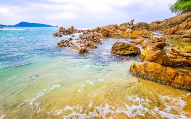 İnanılmaz kayalık Kalim Sahili tropikal manzara manzarası mavi gökyüzü turkuvaz su dalgaları palmiye ağaçları ve kayalar Patong Sahili Kathu Phuket Adası Güney Tayland.