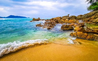 İnanılmaz kayalık Kalim Sahili tropikal manzara manzarası mavi gökyüzü turkuvaz su dalgaları palmiye ağaçları ve kayalar Patong Sahili Kathu Phuket Adası Güney Tayland.