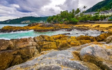 İnanılmaz kayalık Kalim Sahili tropikal manzara manzarası mavi gökyüzü turkuvaz su dalgaları palmiye ağaçları ve kayalar Patong Sahili Kathu Phuket Adası Güney Tayland.