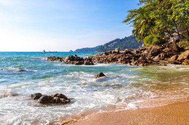İnanılmaz kayalık Kalim Sahili tropikal manzara manzarası mavi gökyüzü turkuvaz su dalgaları palmiye ağaçları ve kayalar Patong Sahili Kathu Phuket Adası Güney Tayland.