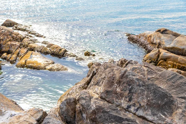 Rocky Kalim Sahili tropikal sahil kıyısı turkuvaz mavisi berrak su dalgaları kum kayaları kaya ve midye kabuklu kayalar Patong Sahili Kathu Phuket Adası Güney Tayland.