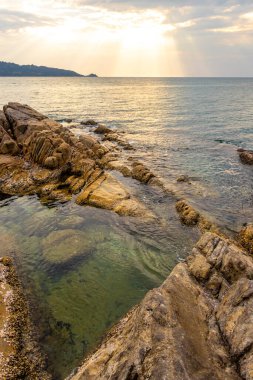 Rocky Kalim Sahili tropikal deniz kıyısı gün batımı güneş doğumu turkuvaz mavisi yeşil su dalgaları kum kayaları ve kayalar Patong Sahili Kathu Phuket Adası Tayland.