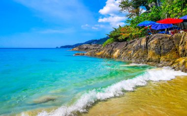 Patong Kamala Sahili Koyu 'nda turistlerle su dalgaları güneş şemsiyeleri tropik bitkiler kayalar ve palmiye ağaçları Güneydoğu Asya' daki Kathu Phuket Adası Eyaleti Tayland 'da.