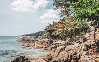 İnanılmaz kayalık Patong Kamala Sahili tropikal manzara manzarası mavi gökyüzü turkuvaz deniz suyu dalgaları palmiye ağaçları ve kayalar Patong Sahili Kathu Phuket Adası Güney Tayland.