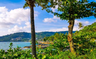 Tropikal Kalim Sahili kayalık sahil kıyısı turkuvaz mavisi berrak su dalgaları kum kayaları ve palmiye ağaçlarının arkasındaki kayalar Patong Sahili Kathu Phuket Adası Tayland.