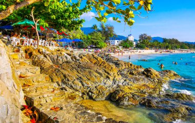 Kathu Bölgesi Phuket Adası, Tayland 25. Şubat 2026 Patong Kamala Sahili Turistlerle su dalgaları güneş şemsiyeleri tropik palmiye ağaçları ve Tayland 'da kayalık merdivenler.