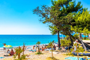 Susanj Bar Belediyesi Karadağ 25. Temmuz 2025 Miejska ve Chico Rico Sahil Koyu turistleri su dalgaları güneş şemsiyeleri tropik bitkiler mavi gökyüzü ve Susanj Bar Karadağ 'daki palmiye ağaçları.