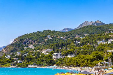 Susanj Bar Belediyesi Karadağ 25. Temmuz 2025 Miejska ve Chico Rico Sahil Koyu turistleri su dalgaları güneş şemsiyeleri tropik bitkiler mavi gökyüzü ve Susanj Bar Karadağ 'daki palmiye ağaçları.