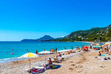 Susanj Bar Belediyesi Karadağ 25. Temmuz 2025 Miejska ve Chico Rico Sahil Koyu turistleri su dalgaları güneş şemsiyeleri tropik bitkiler mavi gökyüzü ve Susanj Bar Karadağ 'daki palmiye ağaçları.