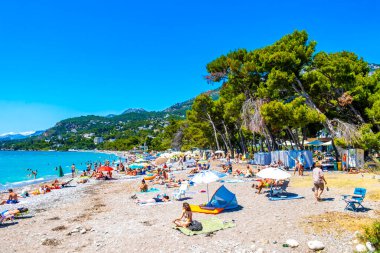 Susanj Bar Belediyesi Karadağ 25. Temmuz 2025 Miejska ve Chico Rico Sahil Koyu turistleri su dalgaları güneş şemsiyeleri tropik bitkiler mavi gökyüzü ve Susanj Bar Karadağ 'daki palmiye ağaçları.