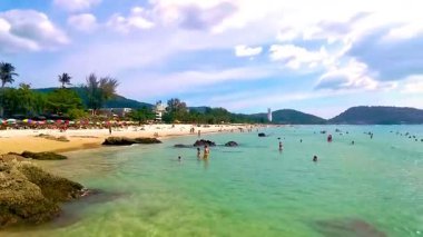 Kathu District Phuket Island Province Thailand 14. February 2026 Patong Kamala Beach bay tourists people water waves sun loungers rock rocks parasols tropical plants and palm trees in Phuket Thailand.