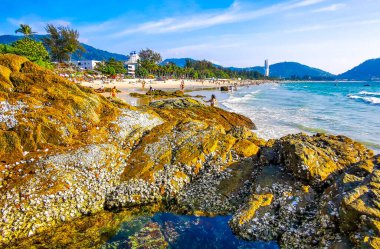 Kathu Bölgesi Phuket Adası, Tayland 04. Mart 2026 Patong Kamala Sahil Koyu 'nda turistler su dalgaları güneş şemsiyeleri tropik bitkiler kayalar ve Tayland palmiyeleri.
