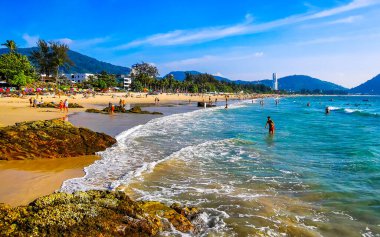 Kathu Bölgesi Phuket Adası, Tayland 04. Mart 2026 Patong Kamala Sahil Koyu 'nda turistler su dalgaları güneş şemsiyeleri tropik bitkiler kayalar ve Tayland palmiyeleri.