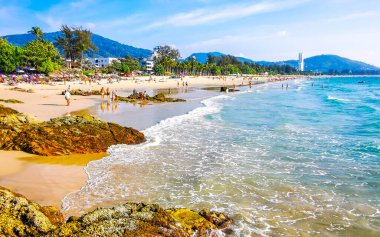 Kathu Bölgesi Phuket Adası, Tayland 04. Mart 2026 Patong Kamala Sahil Koyu 'nda turistler su dalgaları güneş şemsiyeleri tropik bitkiler kayalar ve Tayland palmiyeleri.