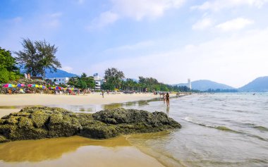 Kathu District Phuket Island Province Thailand 06. March 2026 Patong Kamala Beach bay with tourists people water waves sun loungers parasols tropical plants blue sky and palm trees in Phuket Thailand.