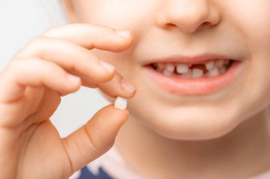 Küçük bir çocuk gülümser ve bir bebek dişini elinde tutar. Çok yakın, yumuşak ışık
