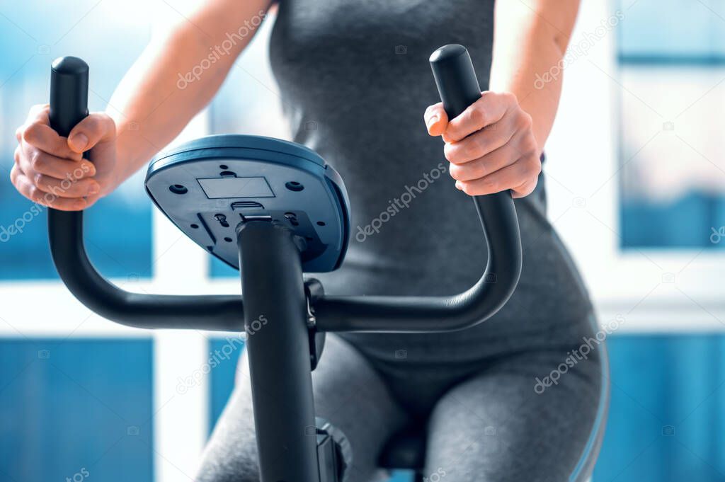 A beautiful athletic girl is engaged on an exercise bike in front of the window at home, front view, close-up. the concept of exercising or losing weight.