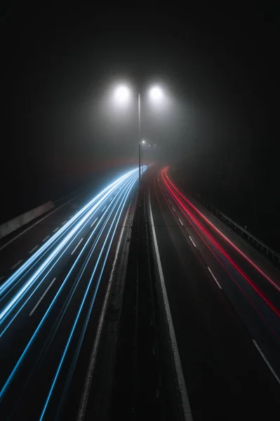 道路上の街灯と夜に湾曲した高速道路上の車のライトトレイルの垂直写真 モーションブラー画像 霧と霧の天気で交通ヘッドライトの動き トップビュー と都市道路 — ストック写真