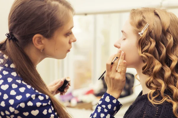 Morena maquillaje artista mujer aplicando maquillaje para un híbrido rubio —  Fotos de Stock