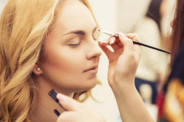 Morena maquillaje artista mujer aplicando maquillaje para un híbrido rubio —  Fotos de Stock