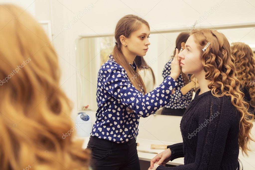 Brunette make up artist woman applying make up for a blonde brid