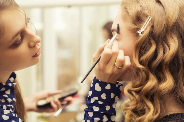 Morena maquillaje artista mujer aplicando maquillaje para un híbrido rubio —  Fotos de Stock