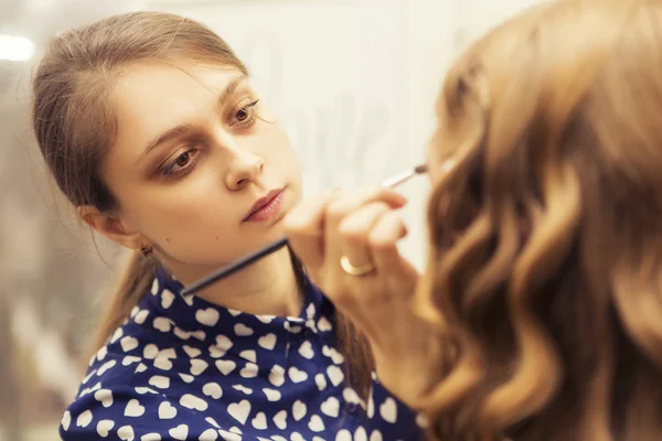 Morena maquillaje artista mujer aplicando maquillaje para un híbrido rubio —  Fotos de Stock